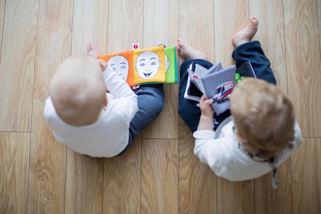 Zwei kleine Kinder sitzen auf dem Boden und schauen Bilderbücher an.